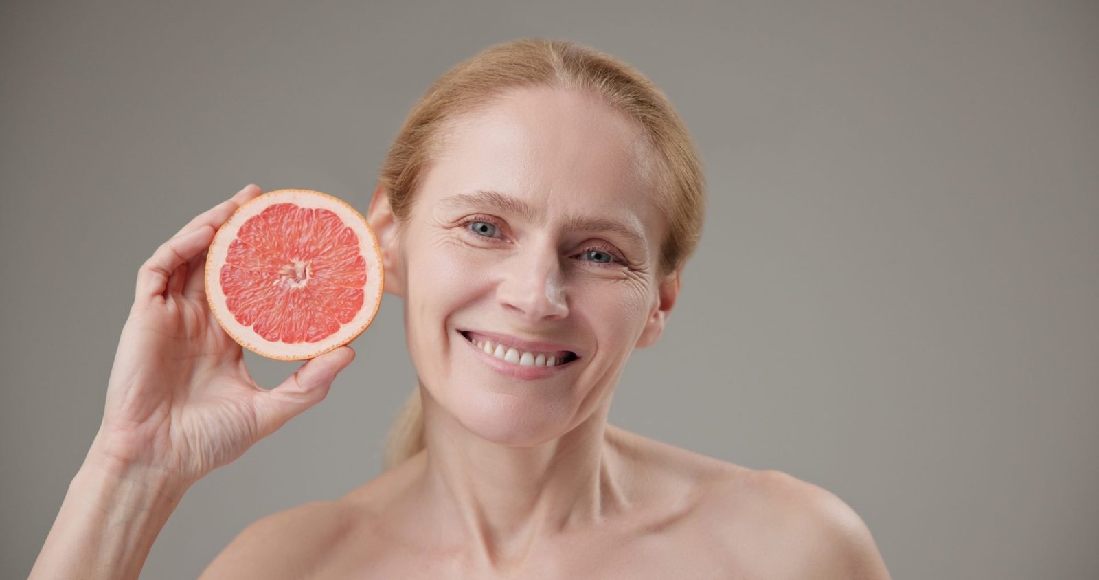 concetto di età, bellezza, salute e skincare routine pelle matura- bella donna caucasica matura di mezza età sulla cinquantina che tiene in mano mezzo pompelmo