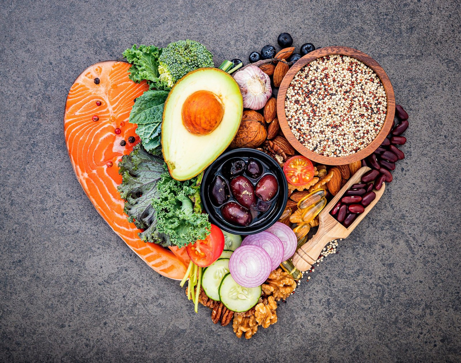 cibi che fanno bene alla pelle- Concetto di dieta chetogenica a basso contenuto di carboidrati a forma di cuore. Ingredienti per una selezione di alimenti sani su sfondo di pietra scura. Ingredienti sani ed equilibrati a base di grassi insaturi per il cuore e i vasi sanguigni.