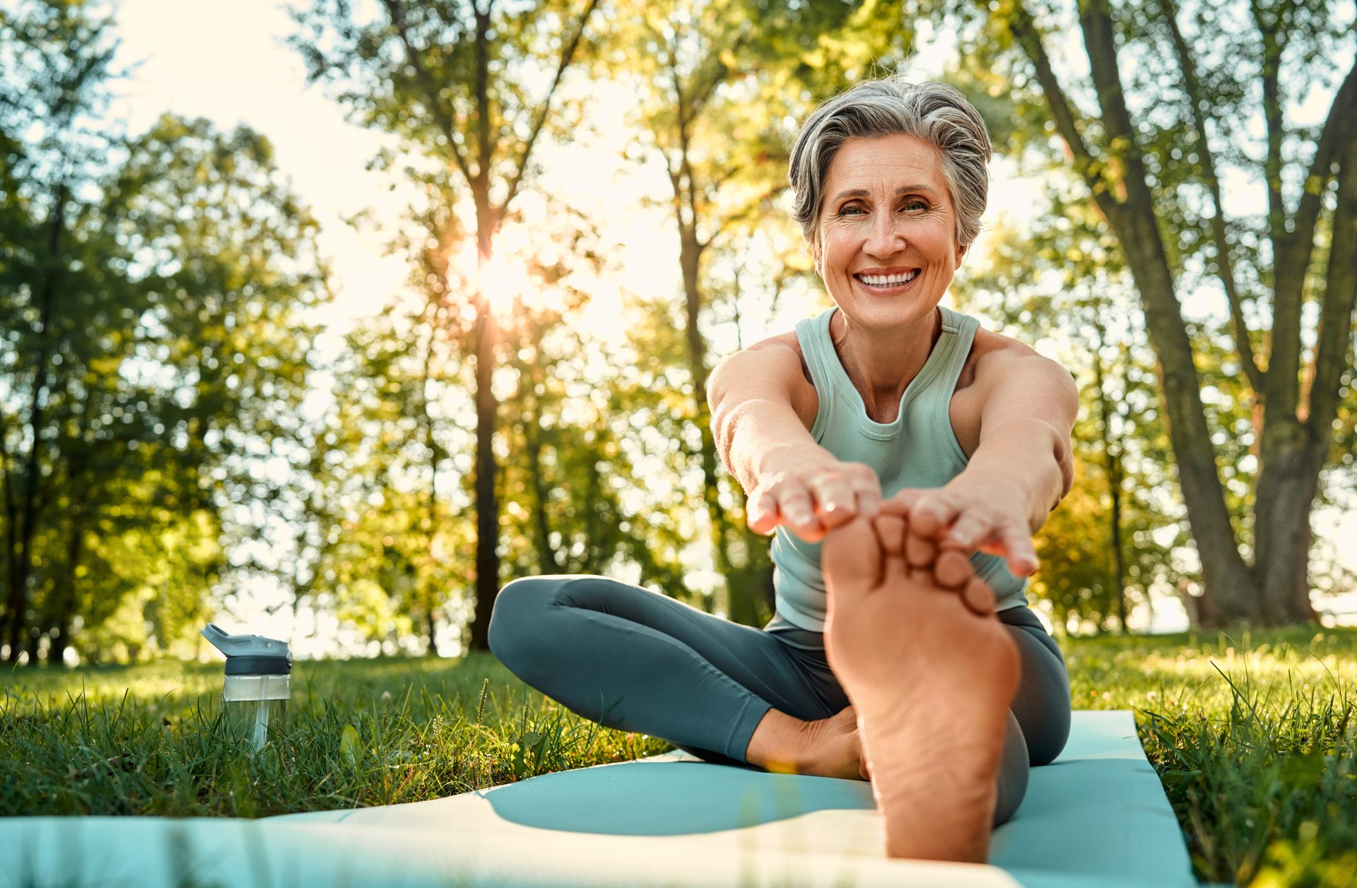 Signora che esegue esercizi di stretching. Ritratto di una signora allegra con un'acconciatura alla moda che si allena all'aperto su un tappetino da yoga e si allunga per toccarsi le dita dei piedi. Una donna anziana dall'aria positiva guarda in camera e sorride. CONCETTO Quale tipo di magnesio assumere in menopausa 