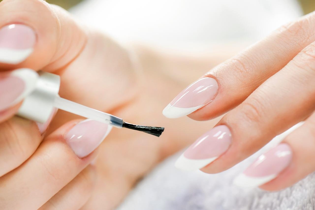 PRIMO PIANO DI MANI DI DONNA CHE APPLICA TOP COAT UNGHIE: CONCETTO DI Come fare una perfetta manicure fai da te su unghie naturali