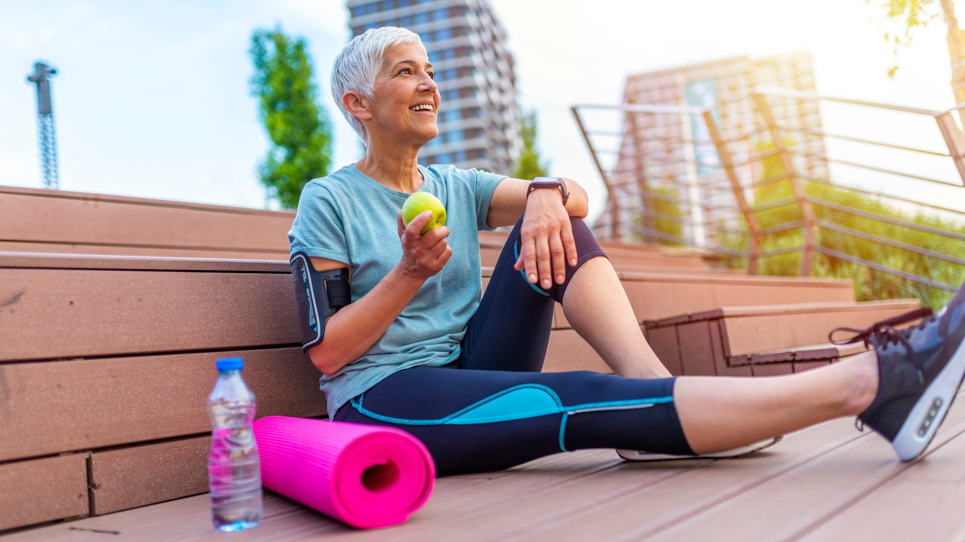 Donna matura e sportiva seduta e rilassata dopo un allenamento o un esercizio, mentre mangia una mela sul pavimento. Concetto di relax. Tema: allenamento di forza e sviluppo muscolare. Bella donna sportiva che mangia una mela. Concetto quale tipo di magnesio assumere in menopausa