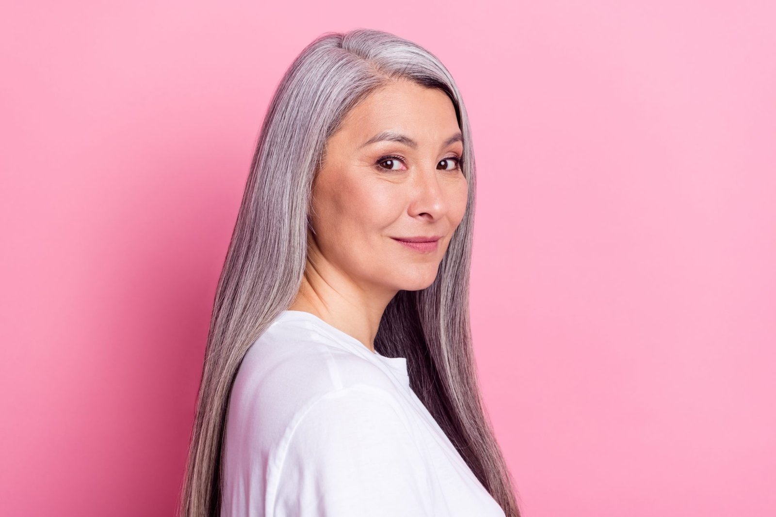 Ritratto fotografico di una donna anziana con i capelli grigi che sorride e indossa abiti casual, isolato su sfondo rosa pastello. Concetto come infoltire i capelli in menopausa