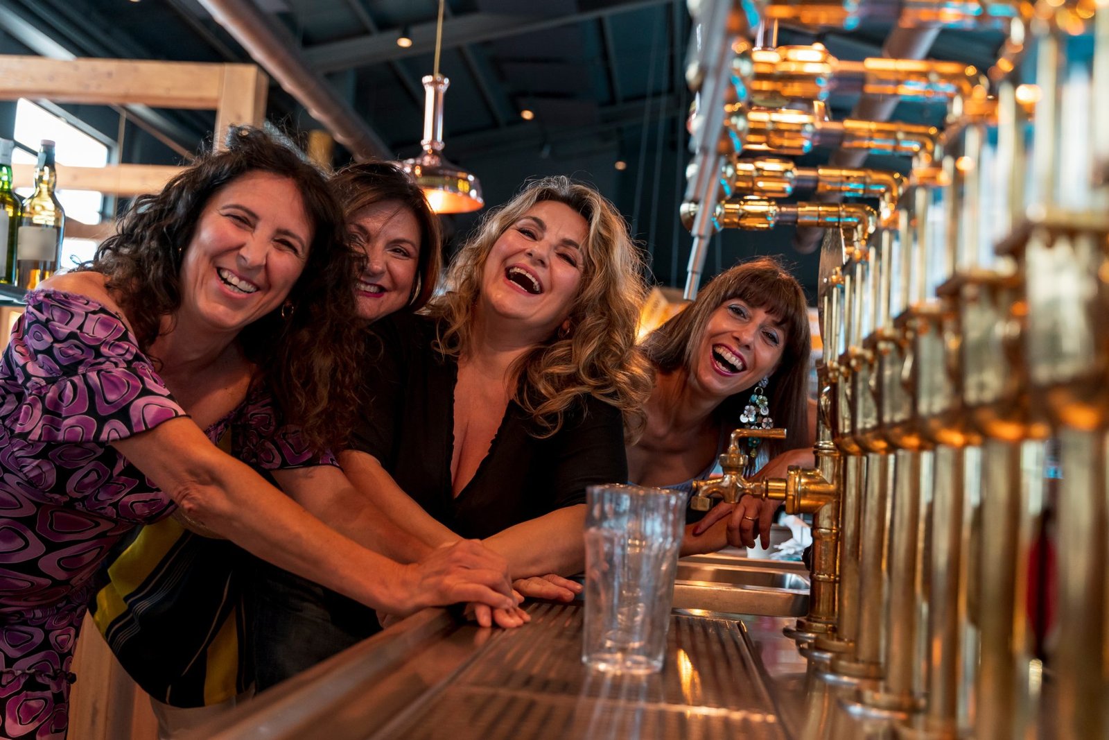 Un gruppo di donne mature sorridenti sta bevendo birra in un pub, davanti a un rubinetto della birra. concetto di come socializzare dopo i 50 anni