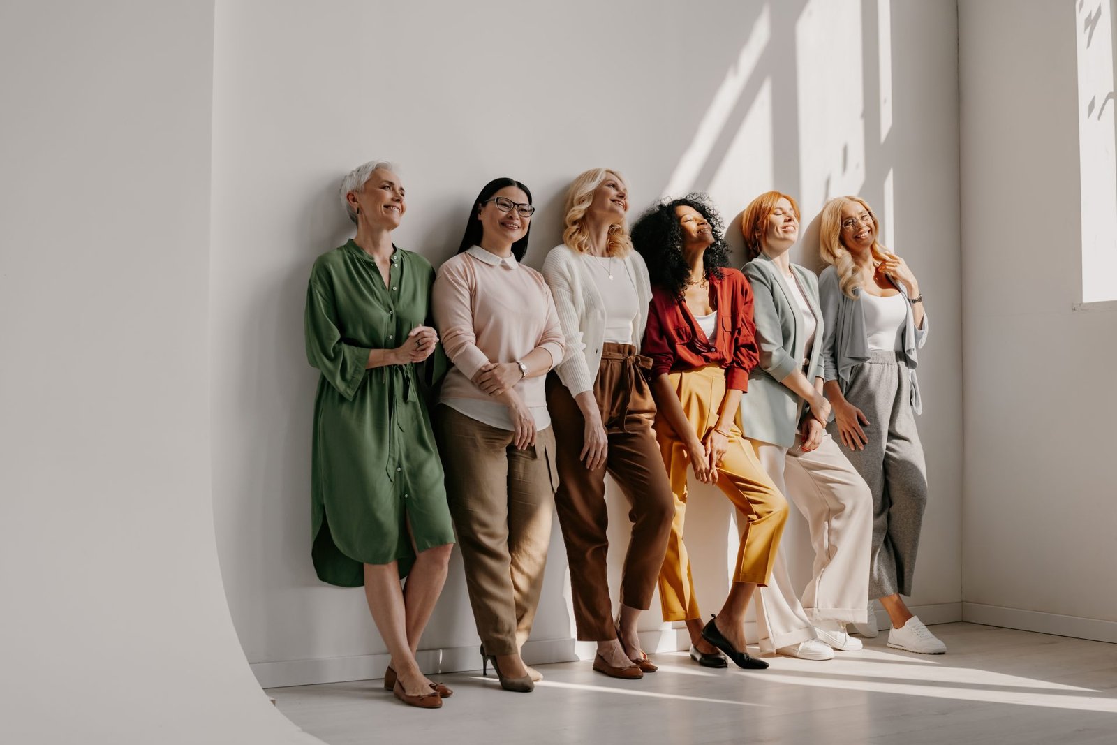 Gruppo multietnico di donne mature che stringono amicizia e sorridono appoggiate insieme al muro. Concetto di come socializzare dopo i 50 anni