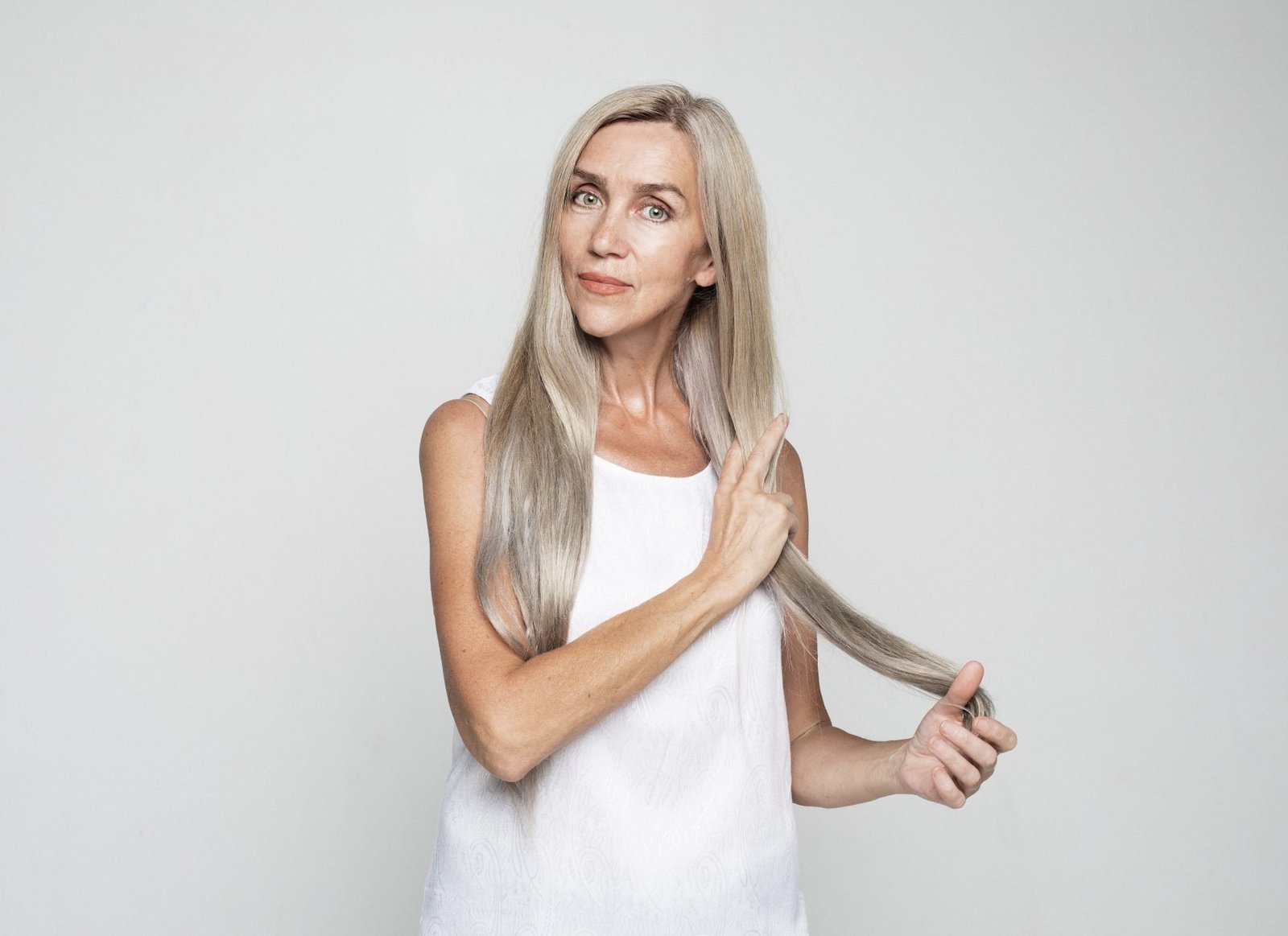 Concetto di bellezza capelli Come infoltire i capelli in menopausa una bella donna matura tocca lunghi e adorabili capelli grigi su sfondo grigio chiaro.