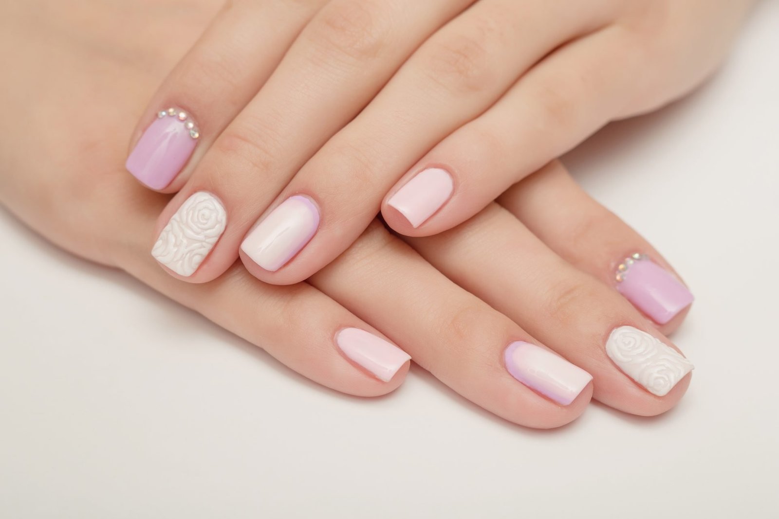 PRIMO PIANO DI MANI CON MANICURE DELICATA E FEMMINILE ROSA E BIANCA - CONCETTO DI UNGHIE CORTE PRIMAVERA 2026