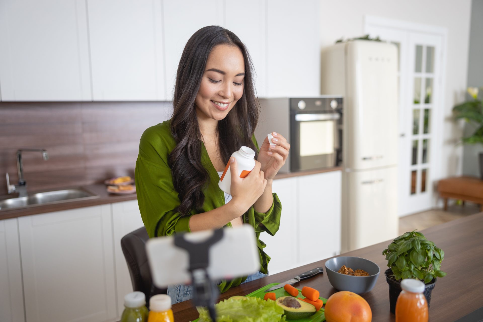 donna assume vitamine nella sua cucina davanti al tavolo con del cibo sano. Concetto QUANDO SONO NECESSARI I MULTIVITAMINICI