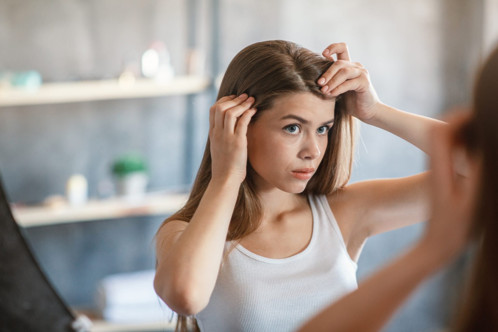 Ragazza millennial con problemi di capelli grassi che si guarda allo specchio a casa. Tema capelli che si sporcano subito 