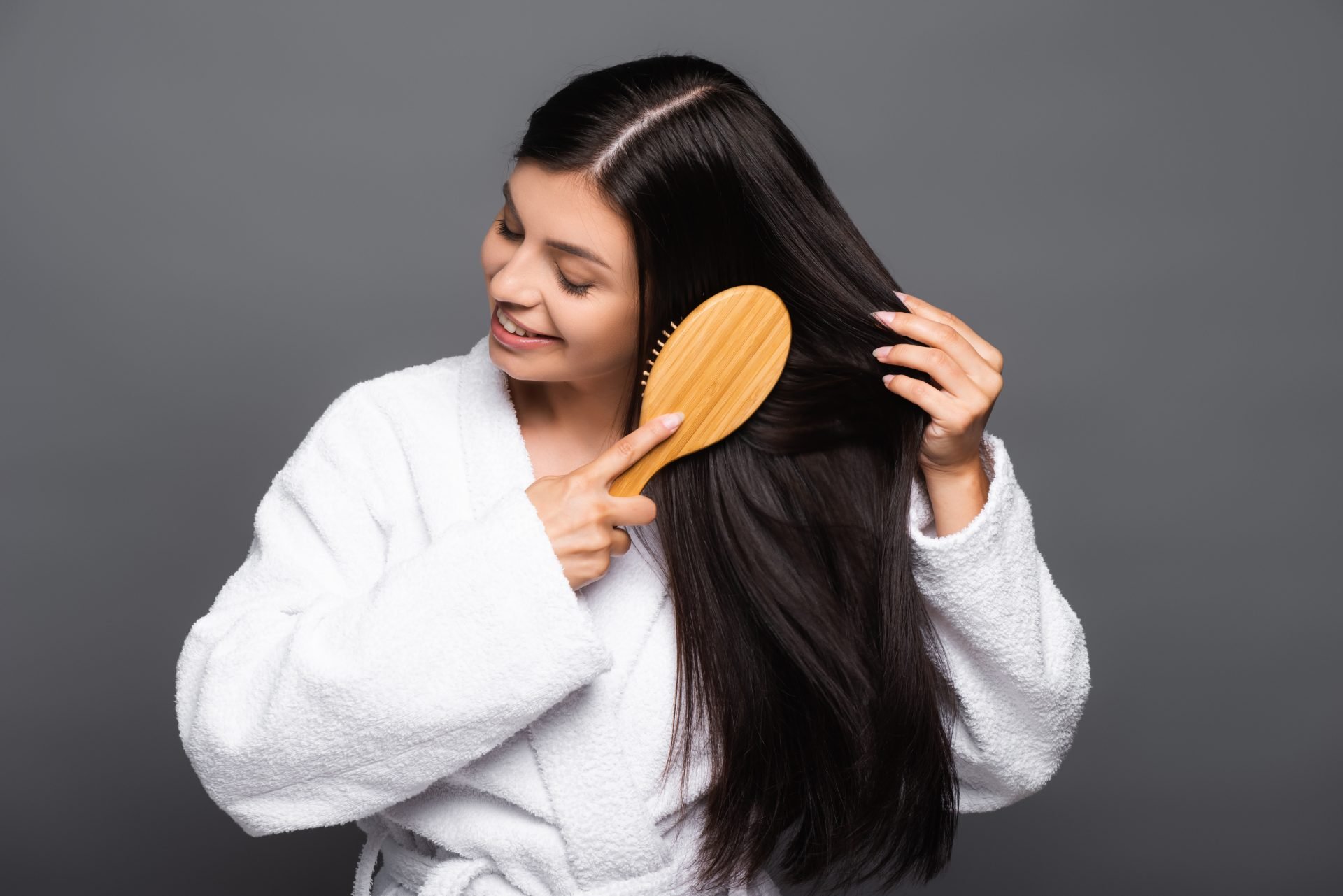 donna bruna in accappatoio che si spazzola i capelli e sorride, isolata su sfondo nero. Tema capelli che si sporcano subito