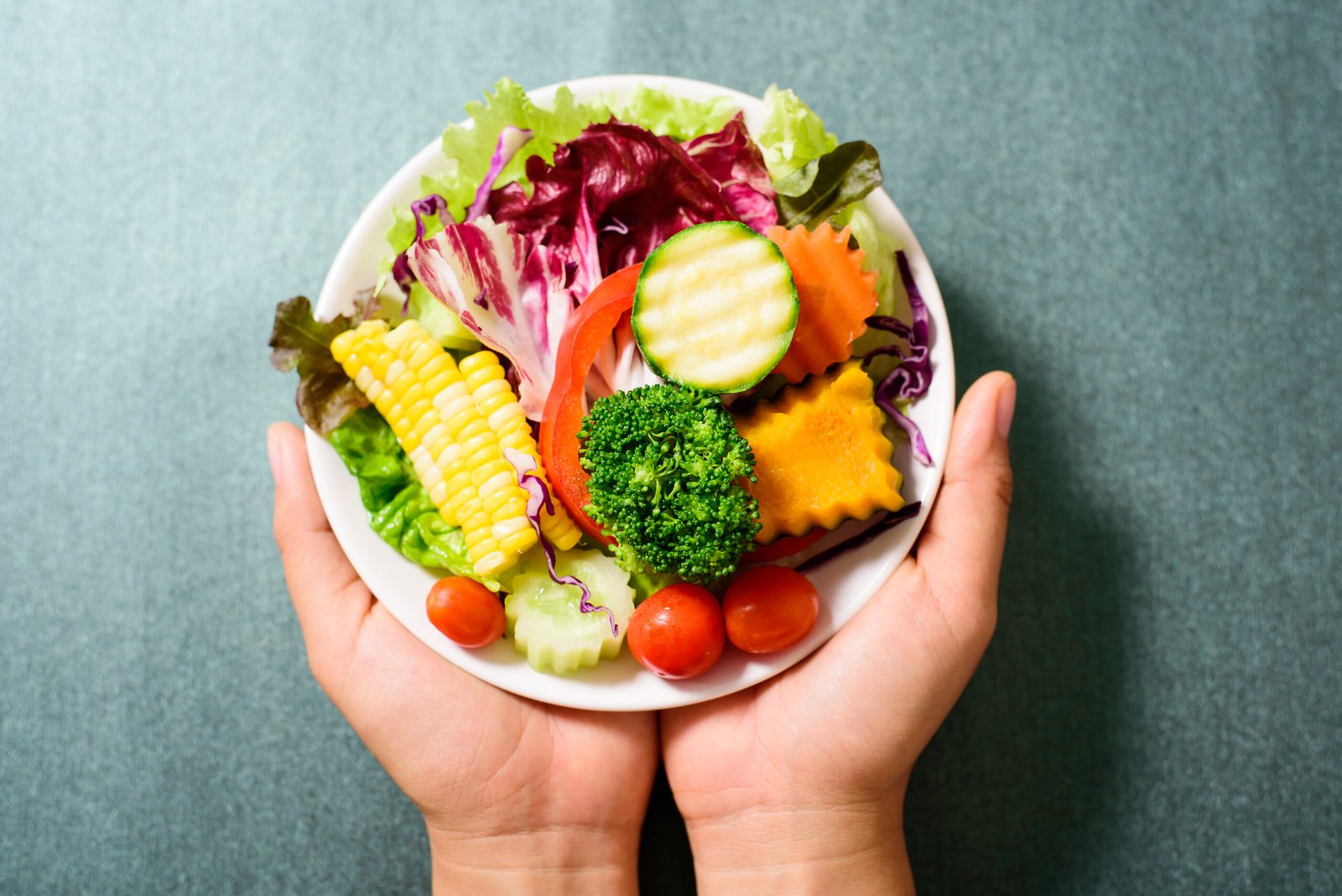 insalata mista di verdure su piatto bianco, tenuta in mano, cibo sano. Primo piano. Concetto di alimentazione sana e correlazione con la salute di mani e unghie. Concetto di mani e carenze nutrizionali e di unghie e carenze nutrizionali