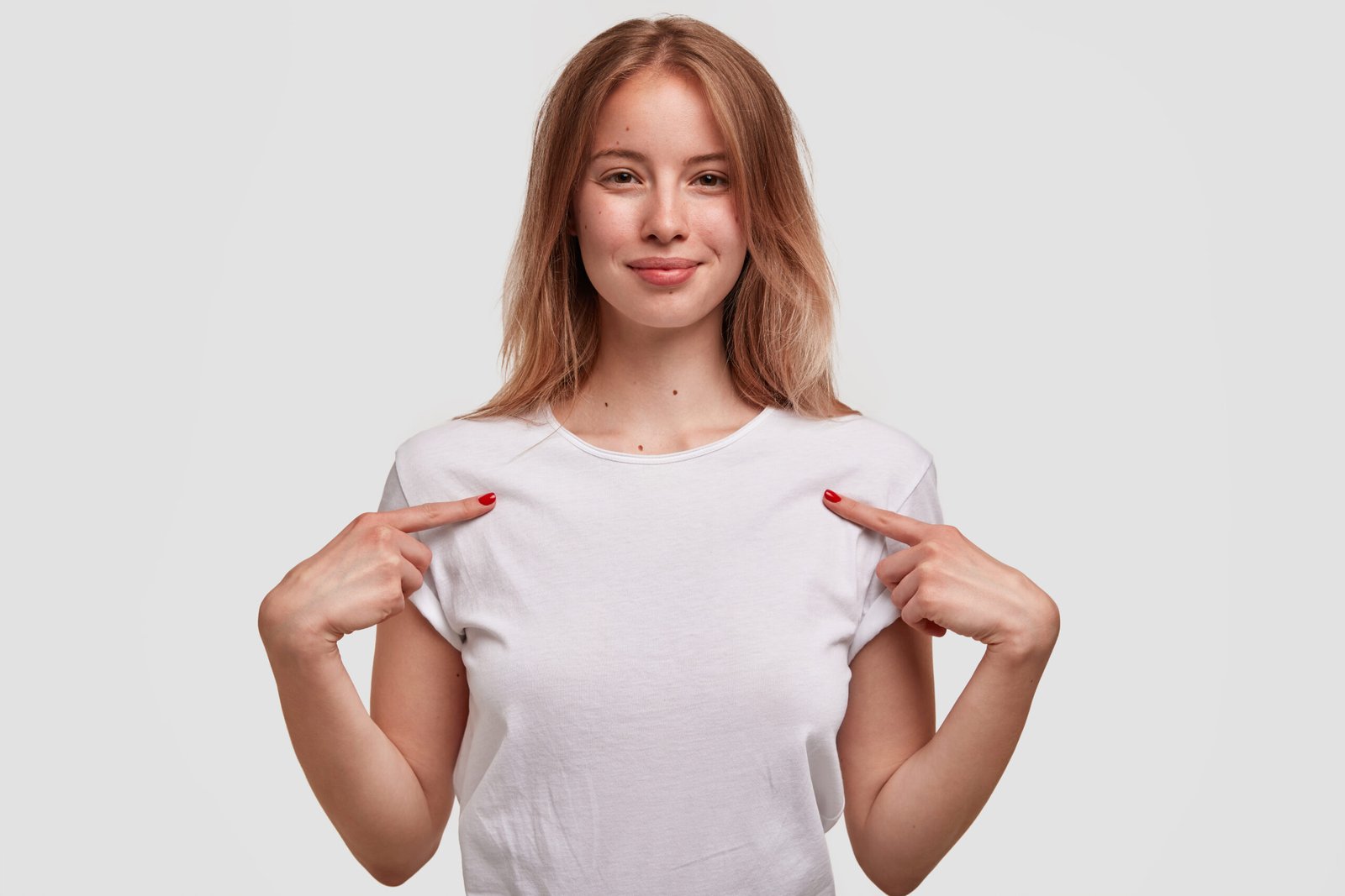 Una graziosa ragazza mostra la sua nuova tshirt binca perfetta, felice dopo l'acquisto, indicando uno spazio vuoto per il tuo contenuto grafico o logo, isolata su sfondo in studio.
