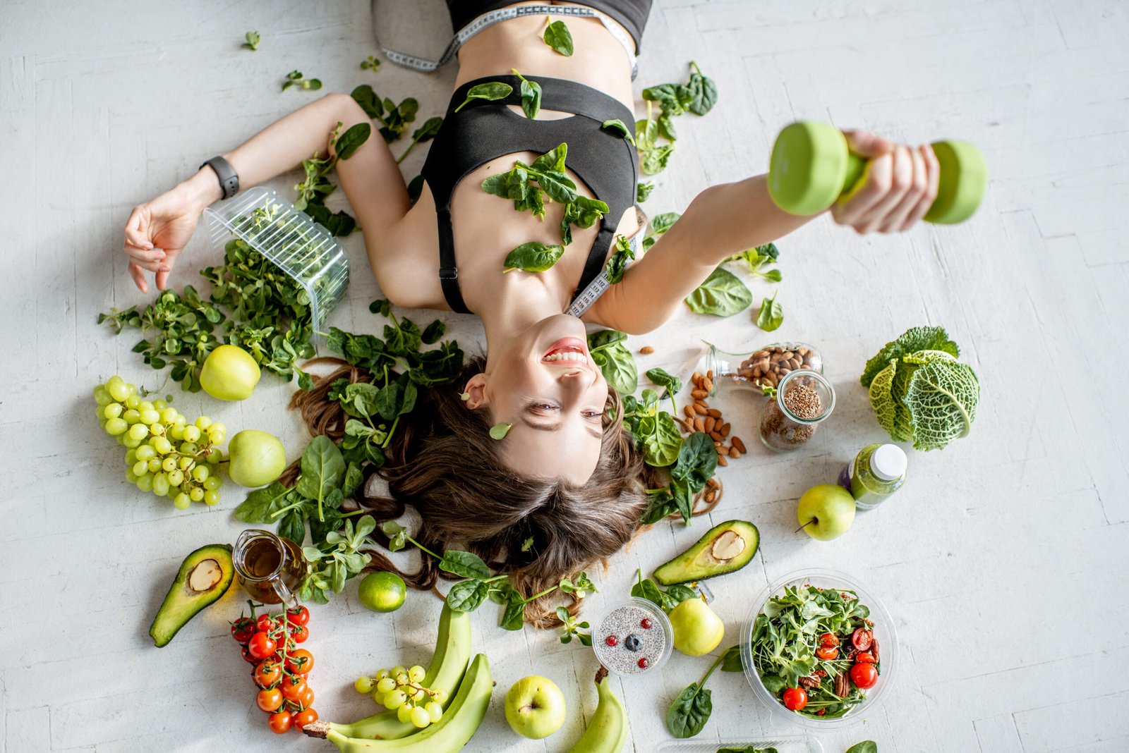 Ritratto di una sportiva circondata da vari alimenti salutari disposti sul pavimento. Concetto di alimentazione sana, cibi che fanno bene alla pelle e stile di vita sportivo.
