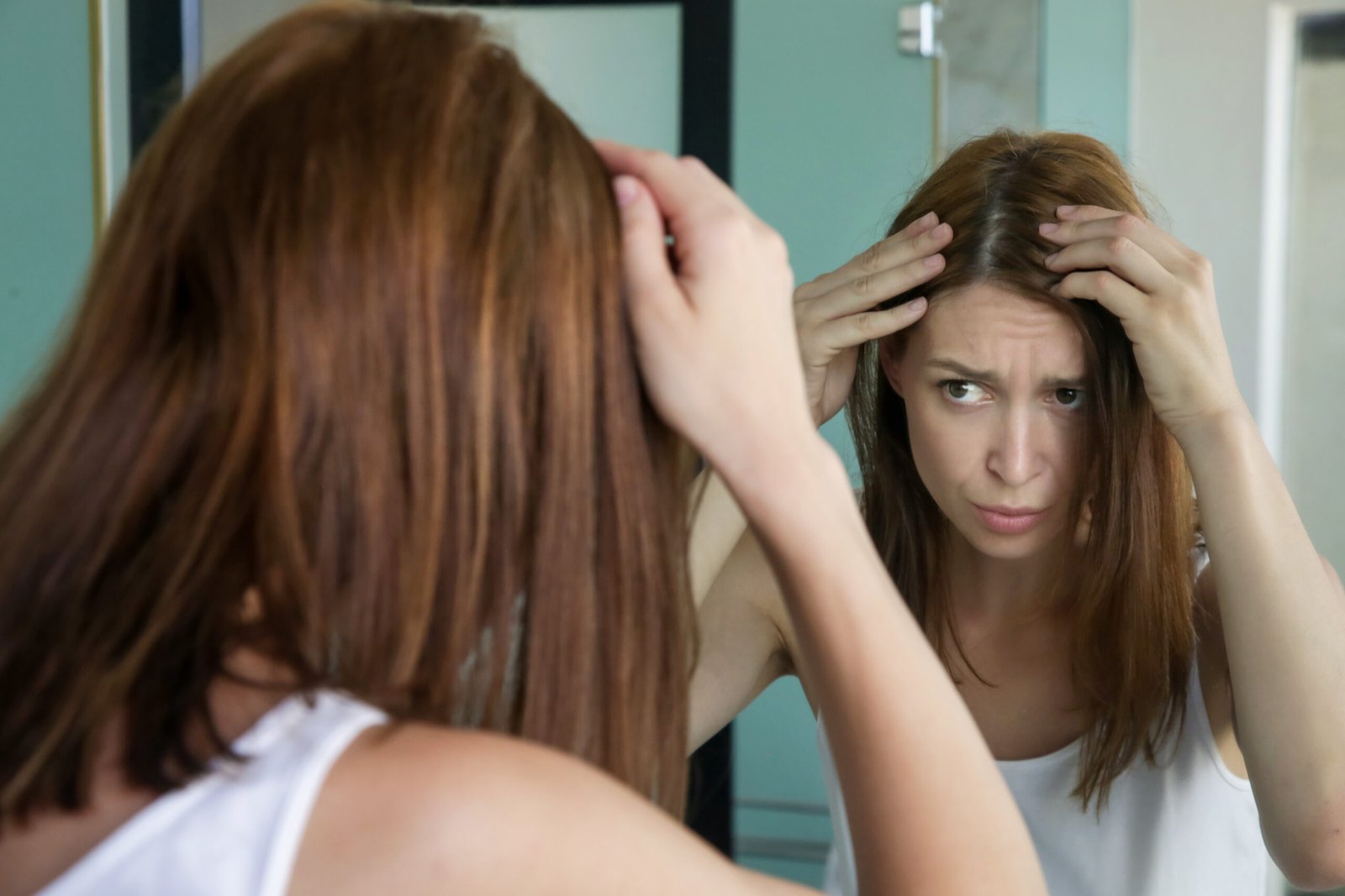 donna allo specchio osserva dispiaciuta la ricrescita di capelli bianchi - concetto di Come coprire i capelli bianchi con la tinta demi permanente