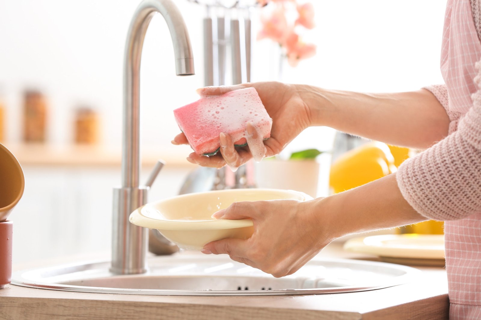 Una donna lava i piatti nel lavello della cucina senza usare guanti protettivi: concetto di mani e problemi alla pelle e unghie. Mani e carenze nutrizionali