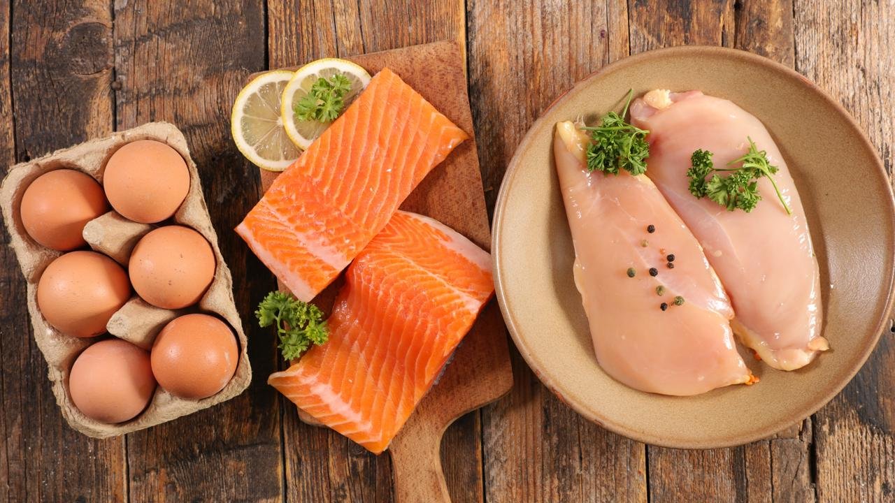 cibi che fanno bene alla pelle: tavola con uova salmone su un tagliere di legno e petto di pollo in un piatto 