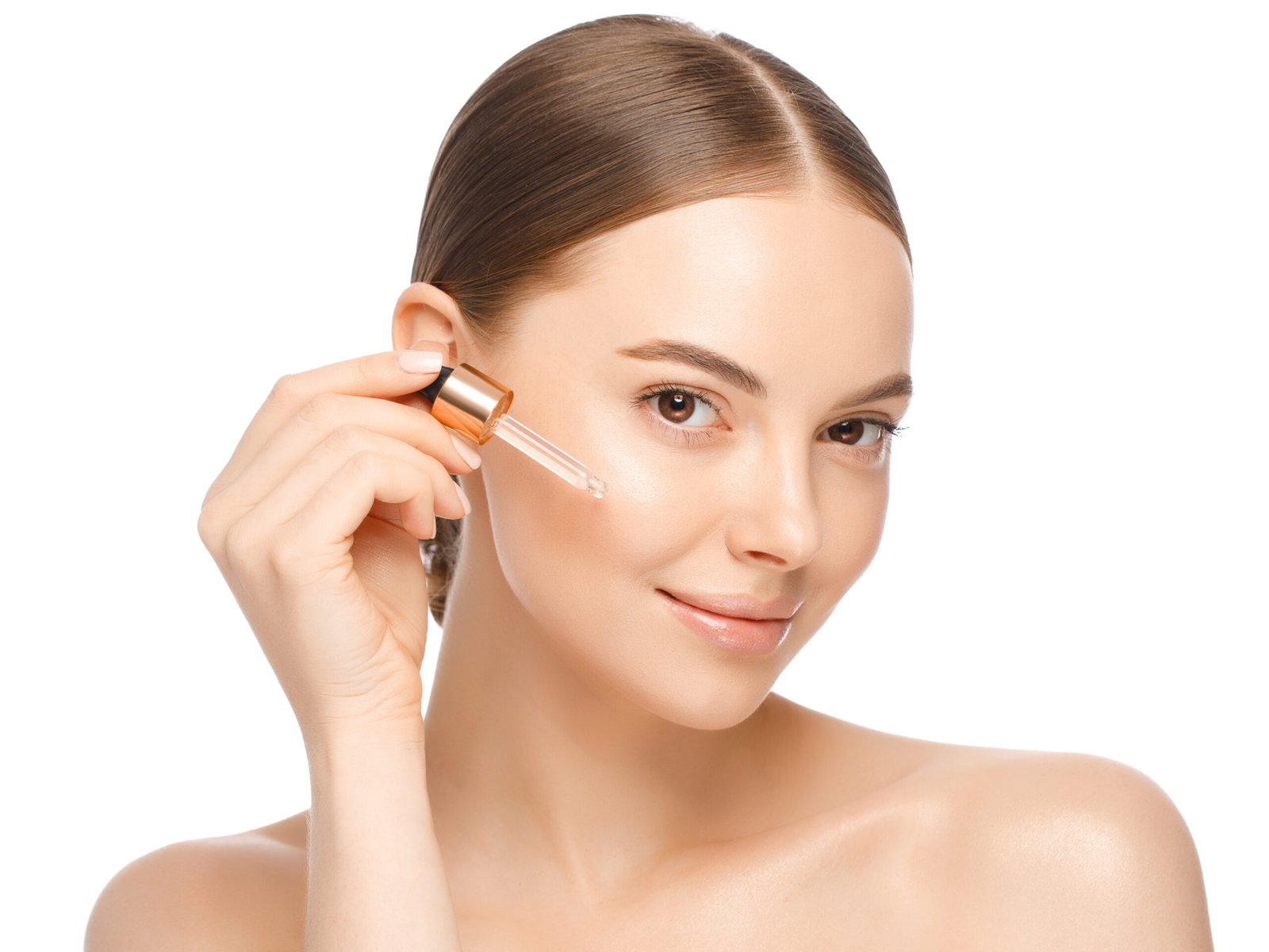 Giovane donna che applica un siero sul viso, guarda in camera, isolata su sfondo bianco. Bellissima modella con una pelle perfetta, pulita e fresca. Pubblicità disiero antiossidante viso per l'estate 