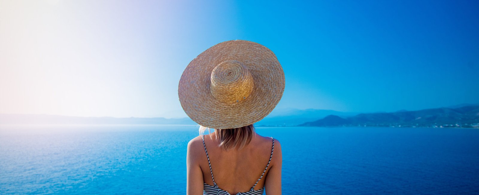 Cappelli per il mare: ragazza con capello di paglia a tesa larga di spalle guarda il mare