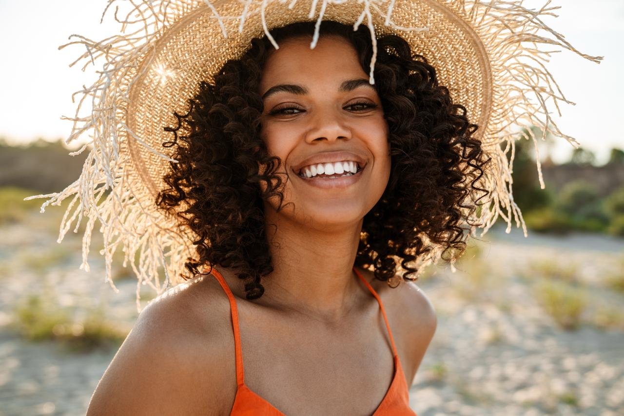 cappelli per il mare ragazza afro sorride col suo cappello di paglia a tesa larga con le frange