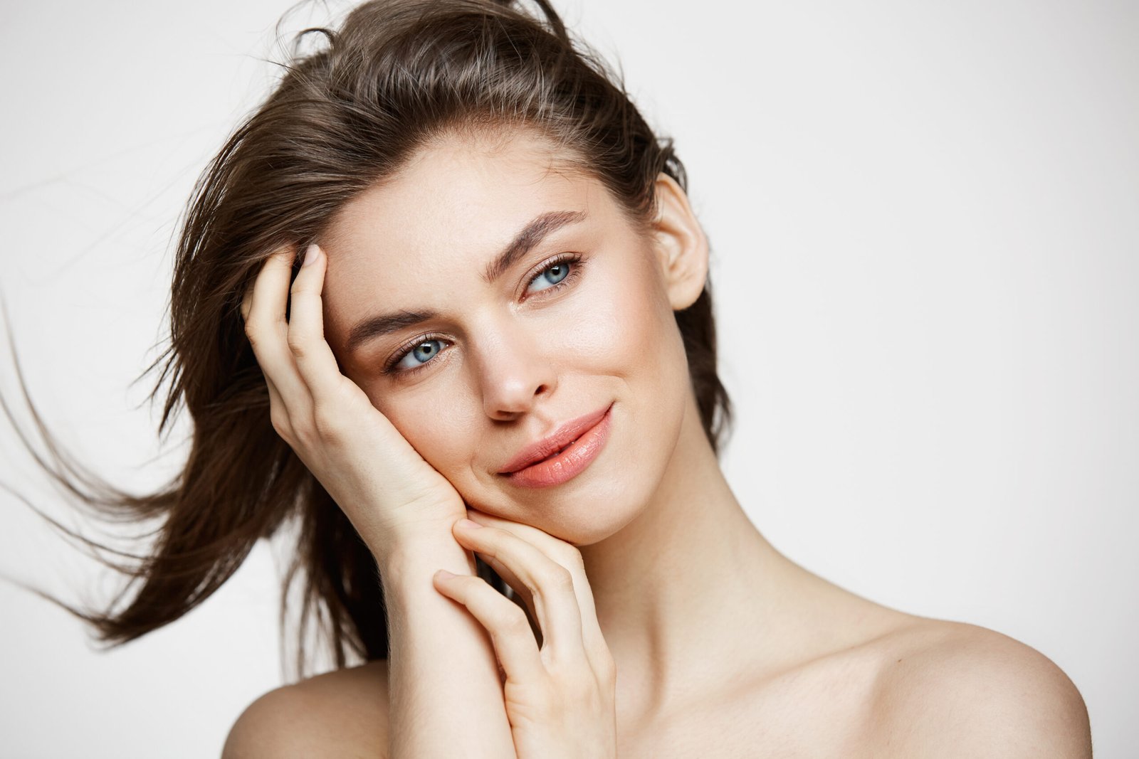Bellissima ragazza nuda con una pelle perfetta e liscia, sorridente mentre si tocca i capelli davanti a un muro bianco. Trattamento viso. barriera utanea