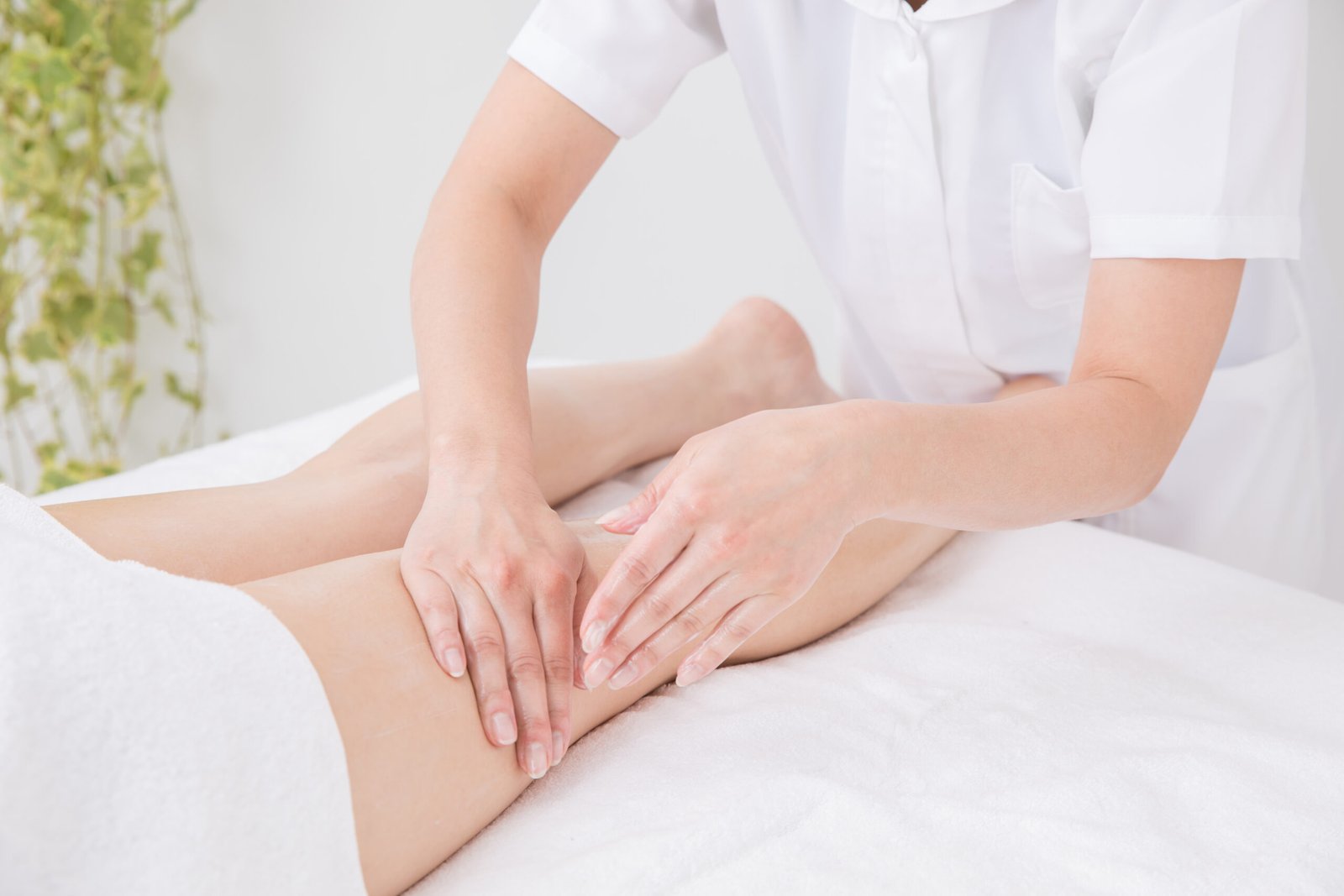 concetto: gambe gonfie e ritenzione idrica. primo piano di mani di una operatrice estetica che fa massaggio linfodrenante a cliente sul lttino