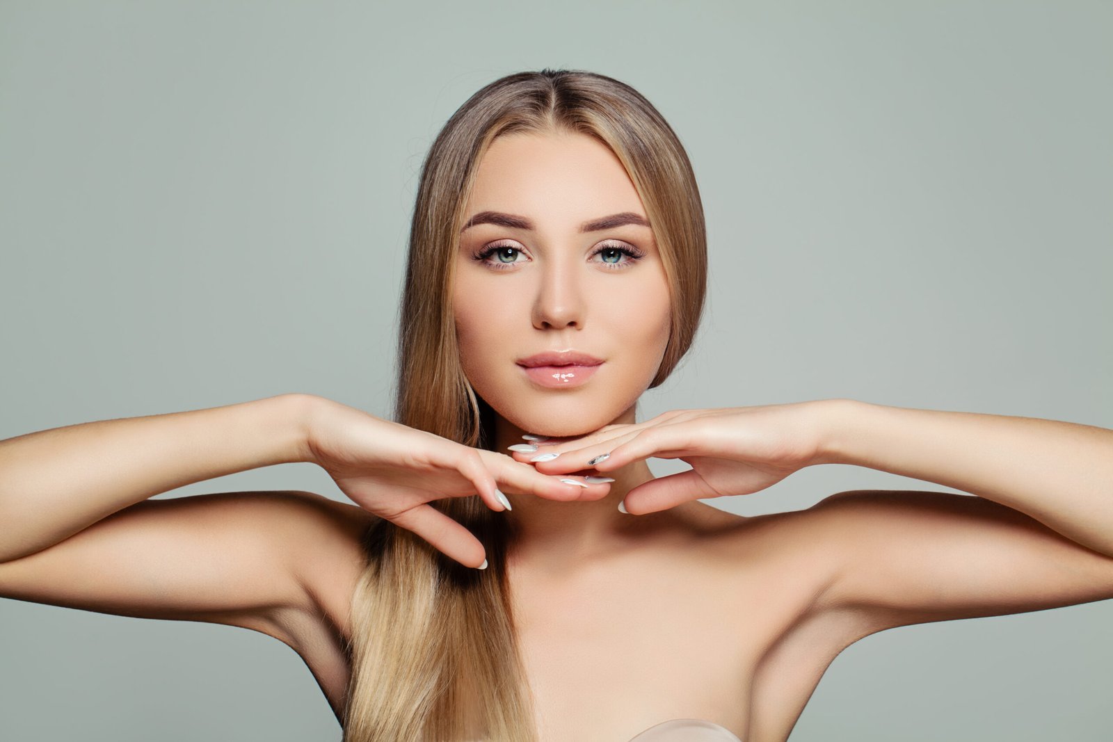 Giovane donna adulta con lunghi capelli lisci e sani e una pelle perfetta e luminosa. Bel viso da modella. Concetto di trattamento viso, cosmetologia, cura dei capelli e della pelle.