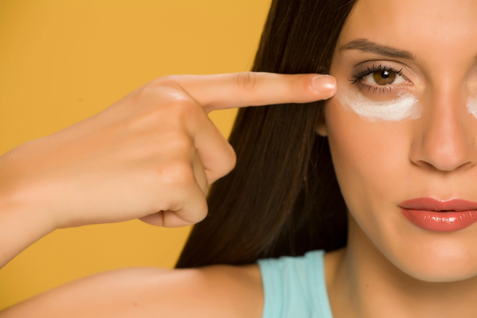 concetto routine skincare mare Giovane donna che applica una crema sulle palpebre inferiori su sfondo giallo