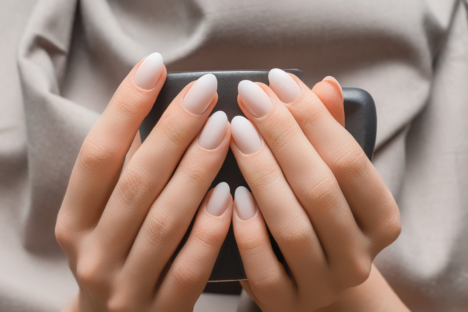 Mani femminili con unghie decorate di bianco. Manicure con smalto bianco. Mani femminili che reggono una tazza di caffè grigia. Concetto unghie estate 2026