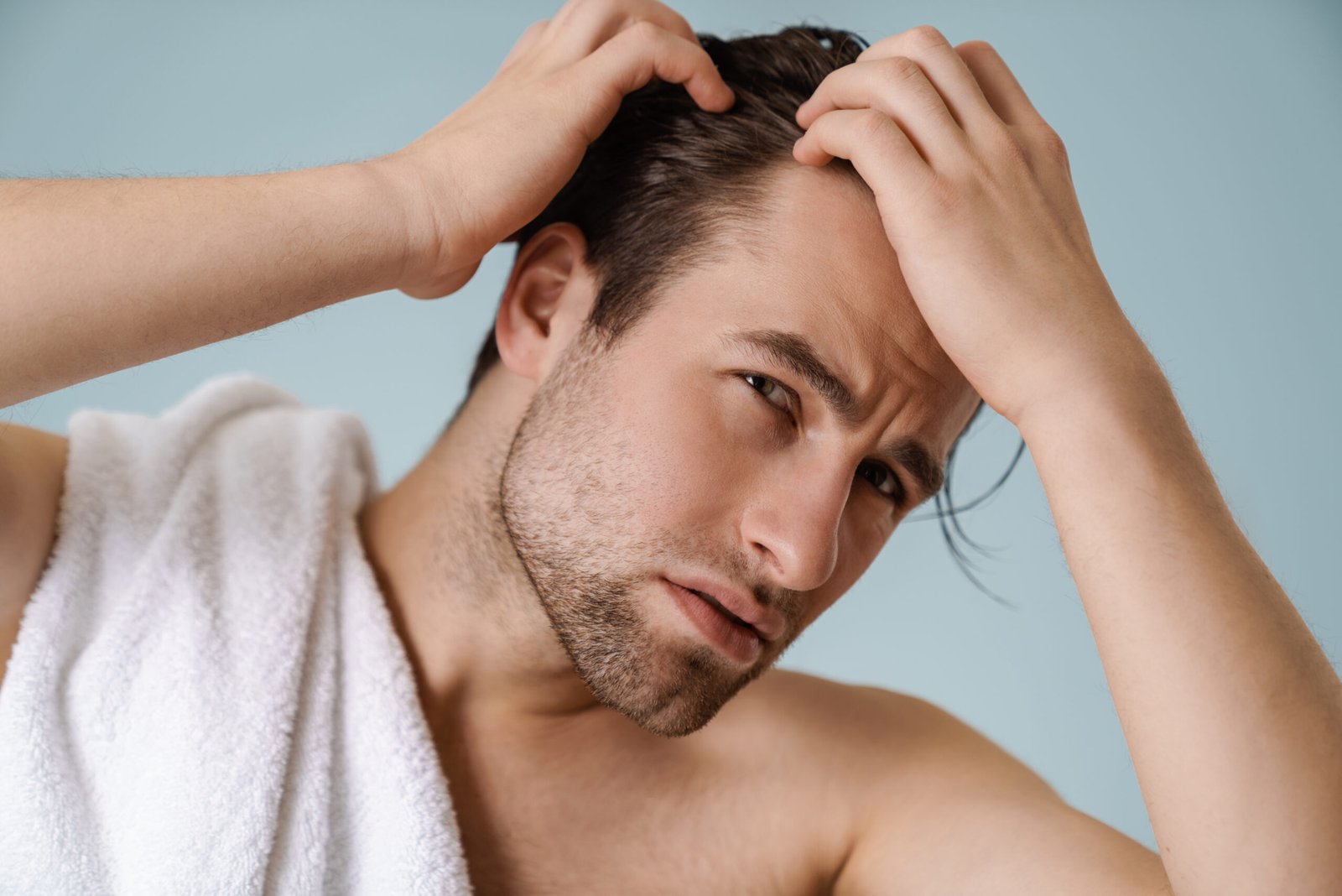 Uomo bianco a torso nudo che si tocca i capelli e guarda in camera, isolato su uno sfondo blu. Concetto haircare, cura e integrazione con Biotina per capelli