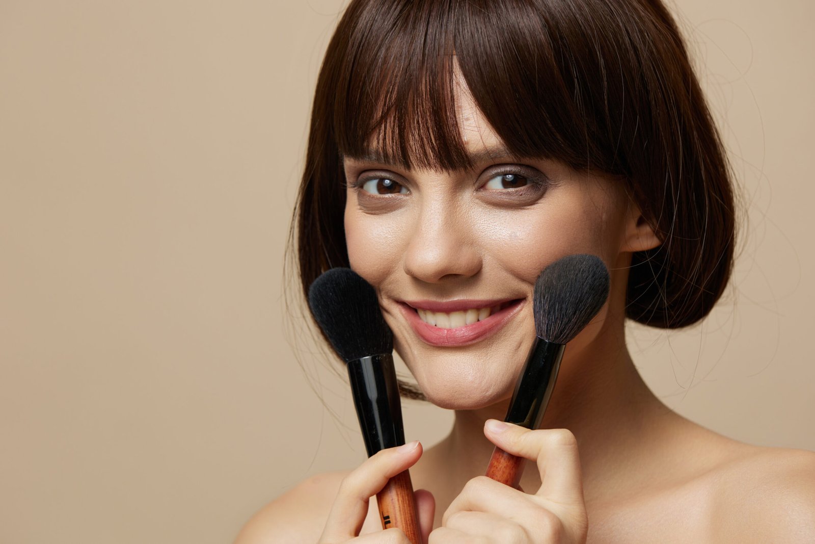 Bellissima donna con pennelli da trucco vicino al viso, spalle scoperte, primo piano, stile di vita. Foto di alta qualità. CONCETTO: Come truccarsi con il caldo in estate -