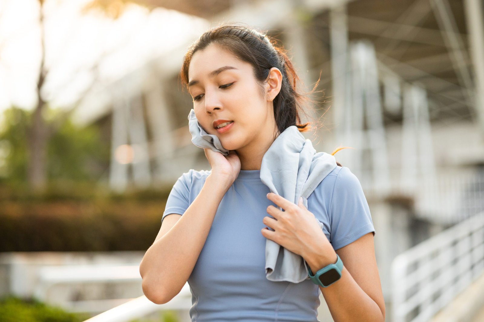 Donna asiatica si asciuga il sudore dal viso e dal collo durante un allenamento in città all'alba. Giovane donna asiatica si prende una pausa dall'allenamento prima della sessione di cardio. Concetto di stile di vita sano e attivo e concetto di Potassio e magnesio quando prenderlI