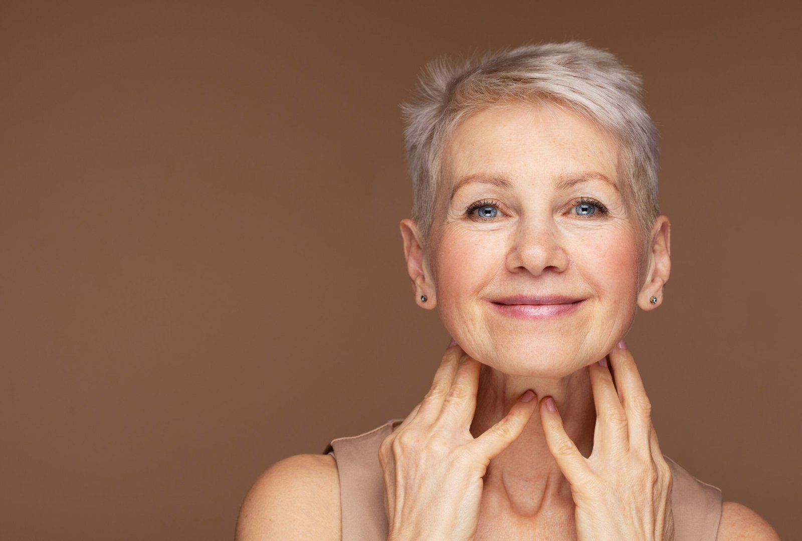 Ritratto di bellezza di una donna matura sorridente con la mano sul viso. Primo piano del volto felice di una donna anziana che si sente ringiovanita dopo un trattamento anti-età. Una bellezza sorridente che guarda in camera con una pelle perfetta. CONCETTO: Come truccarsi con il caldo in estate -