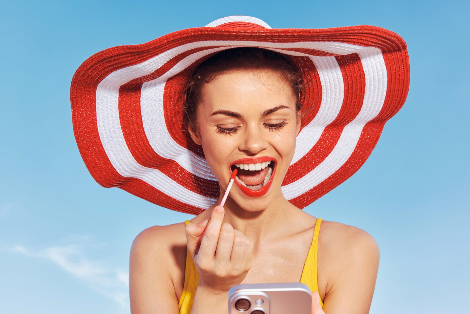 Un'immagine vivace di una donna sorridente con un cappello a tesa larga, che mette in risalto le labbra con un rossetto acceso mentre si gode una giornata di sole all'aria aperta. concetto: Come truccarsi per andare al mare -