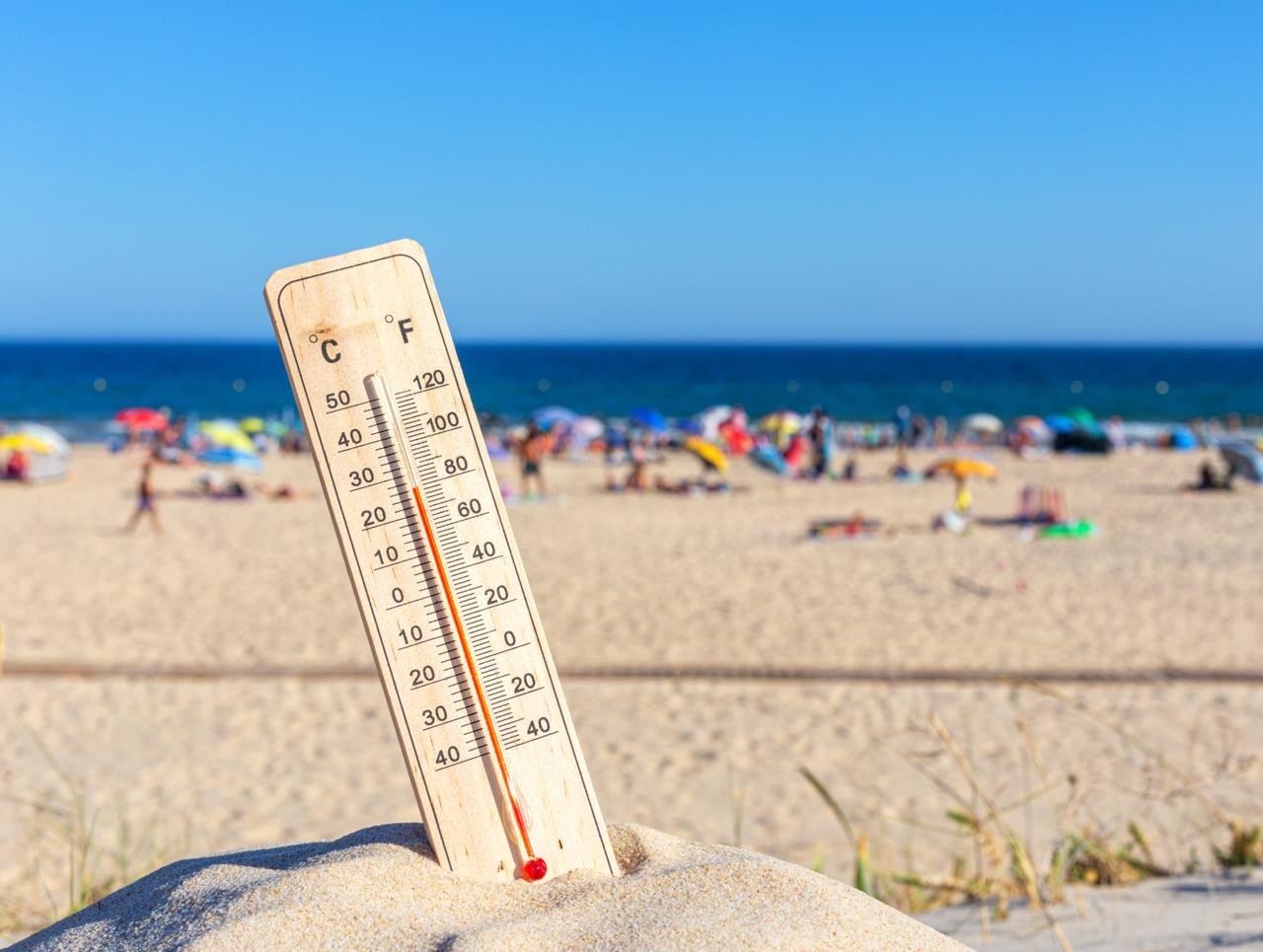 concetto di GAMBE GONFIE E RITENZIONE IDRICA - limitare esposizione al caldo- Immagine di un termomtro in primo piano che segna alta temperatura e sullo sfondo sfuocata una spiaggia