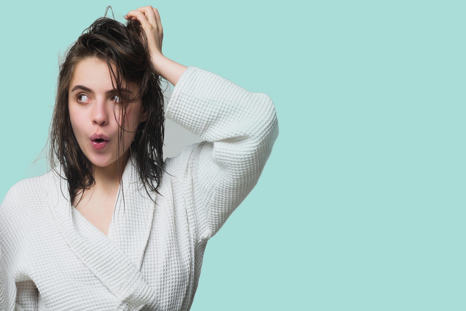concetto di capelli mossi naturali:: ragazza in accappatoio con espressione stupita si tocca i capelli . sfondo isolato
