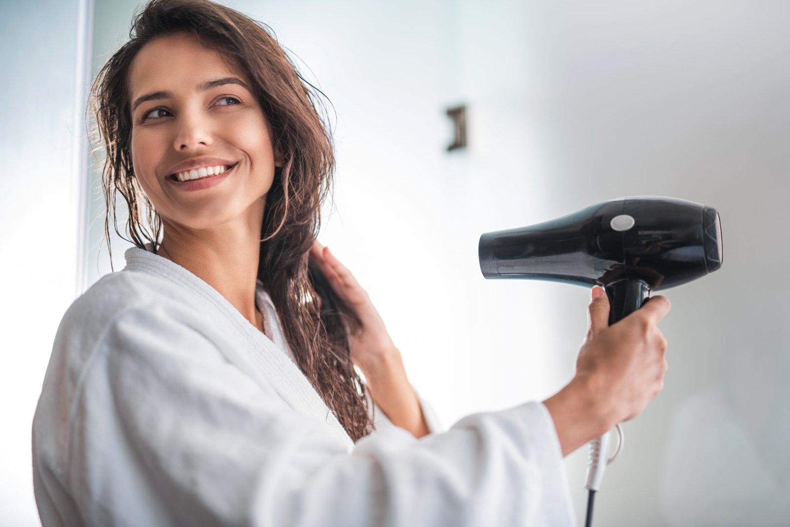 Ritratto di una ragazza sorridente che asciuga i capelli bagnati con un asciugacapelli.