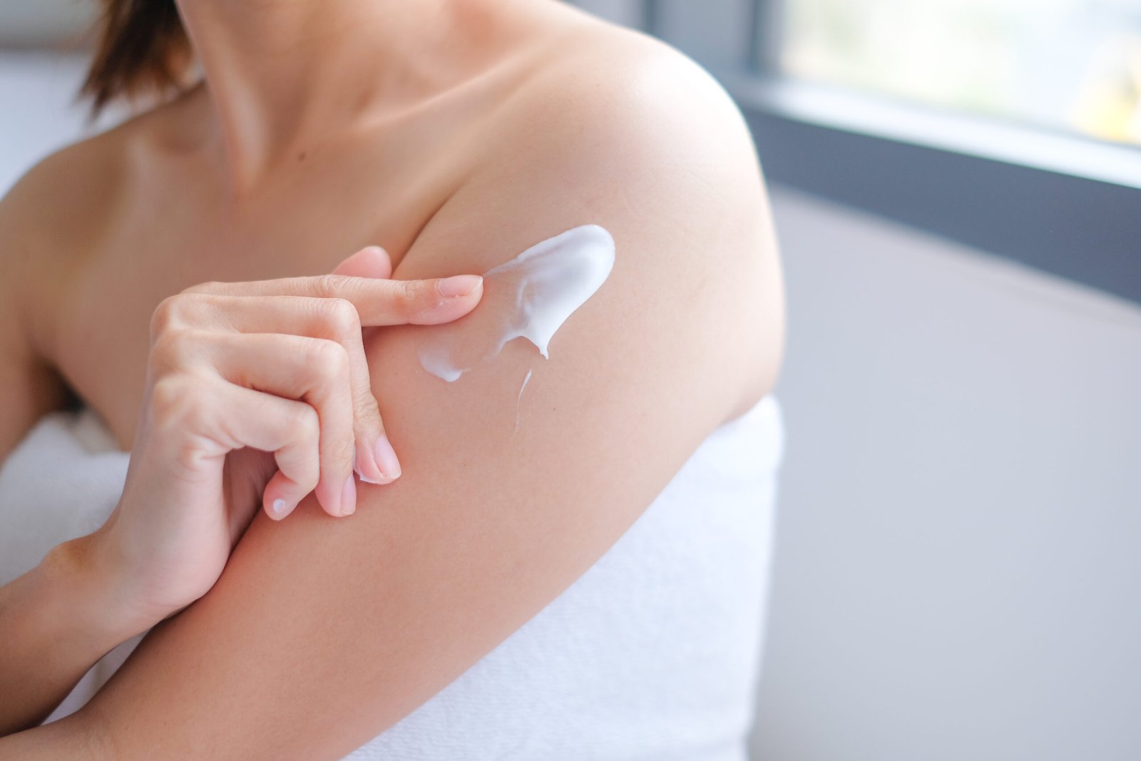 tema idratazione corpo e Migliori creme corpo idratanti e nutrienti. Primo piano dettaglio spalla femminile con mano che una crema
