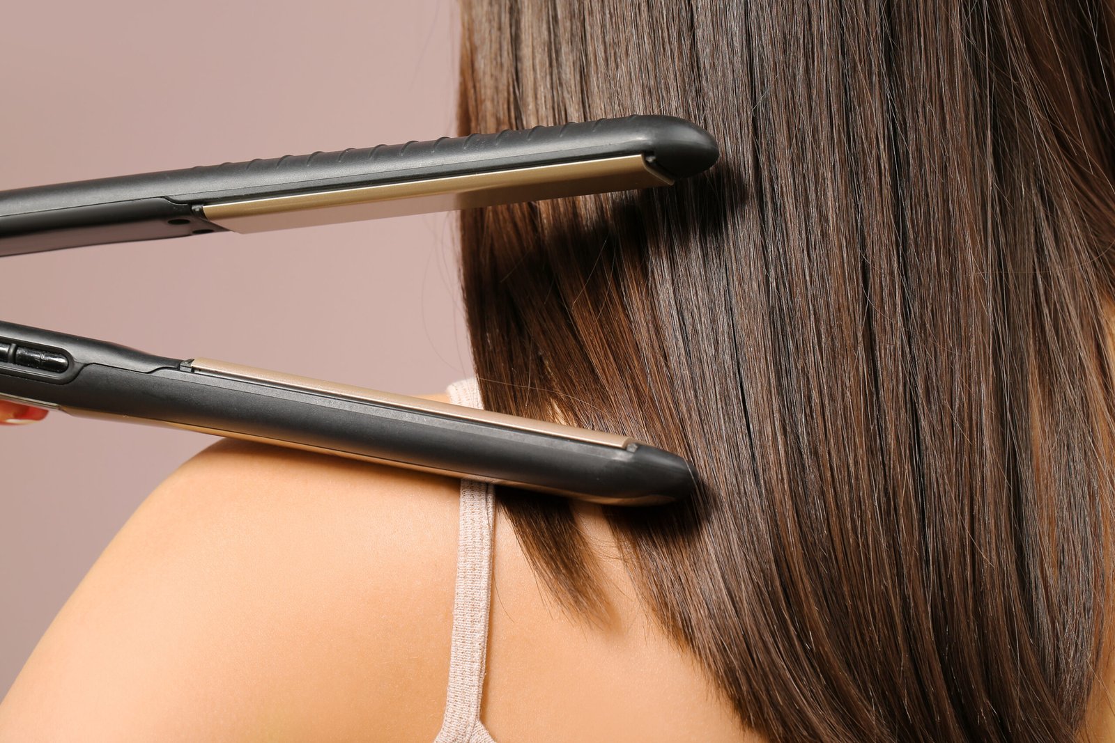 donna di spalle con piastra per capelli su sfondo rosa, primo piano